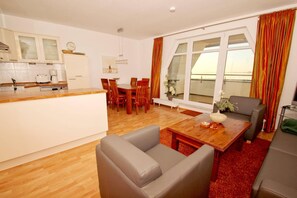 A modern living room with a wooden dining table, grey sofas, and a kitchen area with white cabinets. - Apartment near the harbor with a balcony and a view of the sea - Hafenhäuser Wiek 11 - (Wiek)