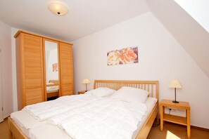 A bedroom with a bed, wooden wardrobe, bedside tables, and a ceiling light. - Apartment near the harbor with balcony and sea view - Hafenhäuser Wiek FeWo 01 - (Wiek)