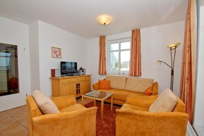 A living room with a sofa set, a television, and a cabinet. - Apartment near the harbor with balcony and sea view - Hafenhäuser Wiek FeWo 01 - (Wiek)