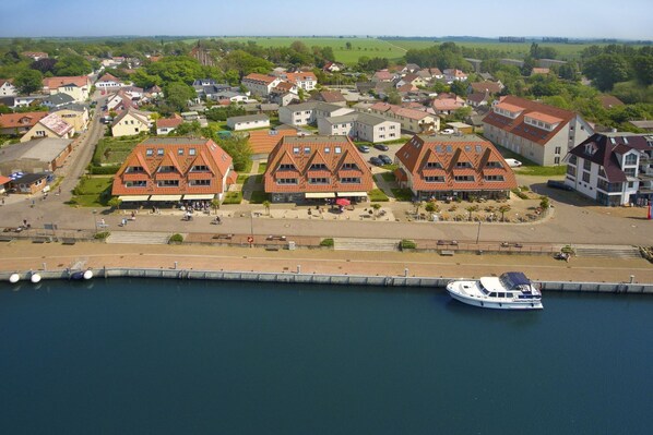 A coastal town with traditional red-roofed buildings, a marina with a boat, and a pedestrian walkway along the waterfront.