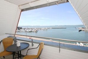 Ein Balkon mit Korbstühlen und einem Tisch mit Blick auf einen Yachthafen, wo Boote und ein Steg liegen.