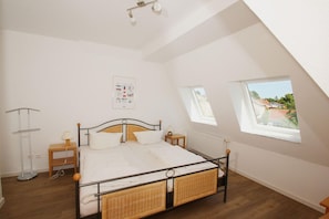 A bedroom with a bed, two bedside tables, a radiator, a window, and a ceiling light fixture.