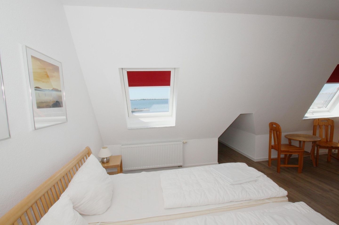 Un dormitorio con cama, escritorio, silla, ventana con persiana roja y radiador.