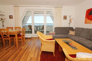 Un salon comprenant un canapé, une table à manger avec des chaises, un fauteuil en osier et une vue sur le balcon.