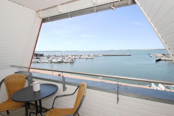 A balcony with wicker chairs and a table, overlooking a marina with boats and a pier.