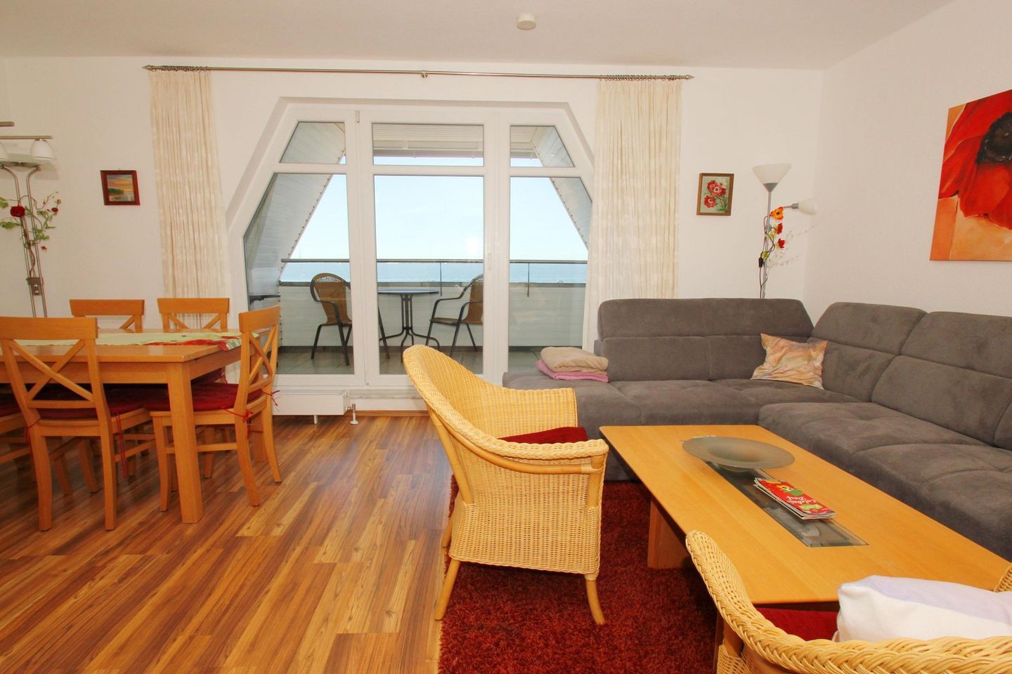 A living room with a sofa, a dining table with chairs, a wicker chair, and a view of the balcony.