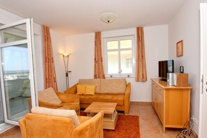 Ein gemütliches Wohnzimmer mit einer Couch, Sesseln, einem Couchtisch, einem Fernseher und einer Holzkassette.
