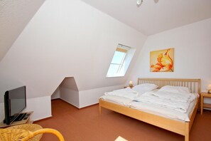 Ein Schlafzimmer mit schrägen Wänden, einem Bett, einem Fernseher, einer Lampe und einem Gemälde.