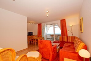 Ein Wohnzimmer mit einer Couch, Sesseln, einem Esstisch und einem Fernseher.