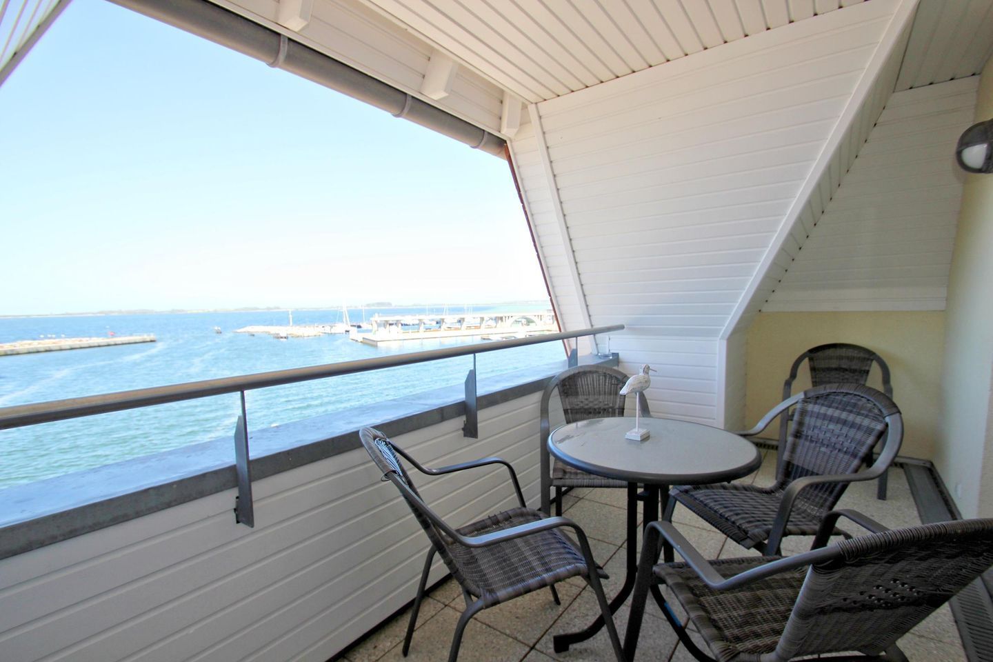 A balcony with a table and chairs, overlooking a marina with boats and a pier.