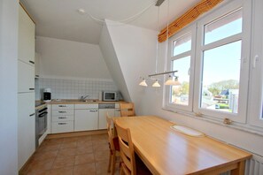 A small kitchen with white cabinets, a microwave, a coffee maker, and a dining table with chairs. There is a window with a view of the outside. - Apartment near the harbor with balcony and sea view - Hafenhäuser Wiek 06 - (Wiek)