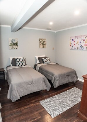 A bedroom with two beds, a patterned rug, and floral wall art.