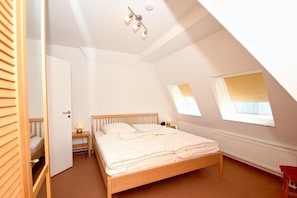 A bedroom with a wooden bed, a nightstand, a lamp, and a window.