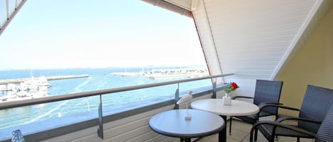 A balcony with a view of the sea, featuring two round tables and wicker chairs.