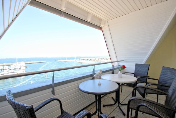 A balcony with a view of the sea, featuring two round tables and wicker chairs.