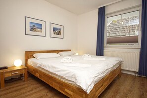 Ein ordentlich bezogenes Bett mit weißen Leinen und Handtüchern, ein hölzerner Kopfseitenverkleidung, eine Nachttischlampe und zwei gerahmte Bilder an der Wand.