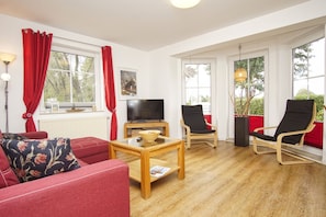 Ein Wohnzimmer mit einem roten Sofa, einem Holztisch, einem schwarzen Sessel und einem Fernseher.