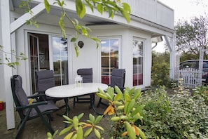 A white building with a patio area featuring a round table and four chairs. - Neptun Apartment - comfortable 3-room apartment with a terrace and garden - (Breege)