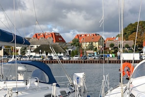 Ein Yachthafen mit vertäuten Booten, eine Pier mit Autos und im Hintergrund Gebäude mit roten Dächern.