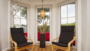 Deux fauteuils noirs à coussins, dotés d’une structure en bois, se trouvent dans une pièce avec de grandes fenêtres et un luminaire suspendu.