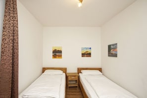 A small, clean room with two single beds, a wooden nightstand, and three wall-mounted paintings.