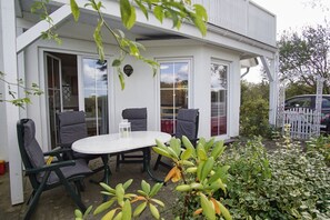 A white building with a patio area featuring a round table and four chairs. - Apartment Neptun - cozy 3-room apartment with terrace and garden - (Breege)