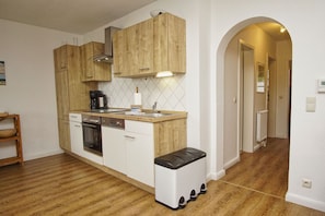 A compact kitchen with wooden cabinets, a built-in oven, and a countertop with a coffee maker. - Neptun Apartment - comfortable 3-room apartment with a terrace and garden - (Breege)