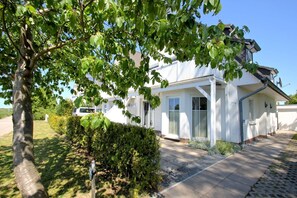 A white two-story house with a covered porch, a driveway, and a hedge in front. - Apartment Neptun - cozy 3-room apartment with terrace and garden - (Breege)