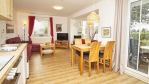 Un salon moderne avec une table et des chaises en bois, un canapé, un téléviseur et une grande fenêtre avec des rideaux.