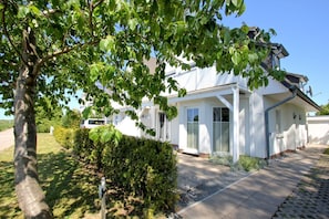 A white two-story house with a covered porch, a driveway, and a hedge in front.