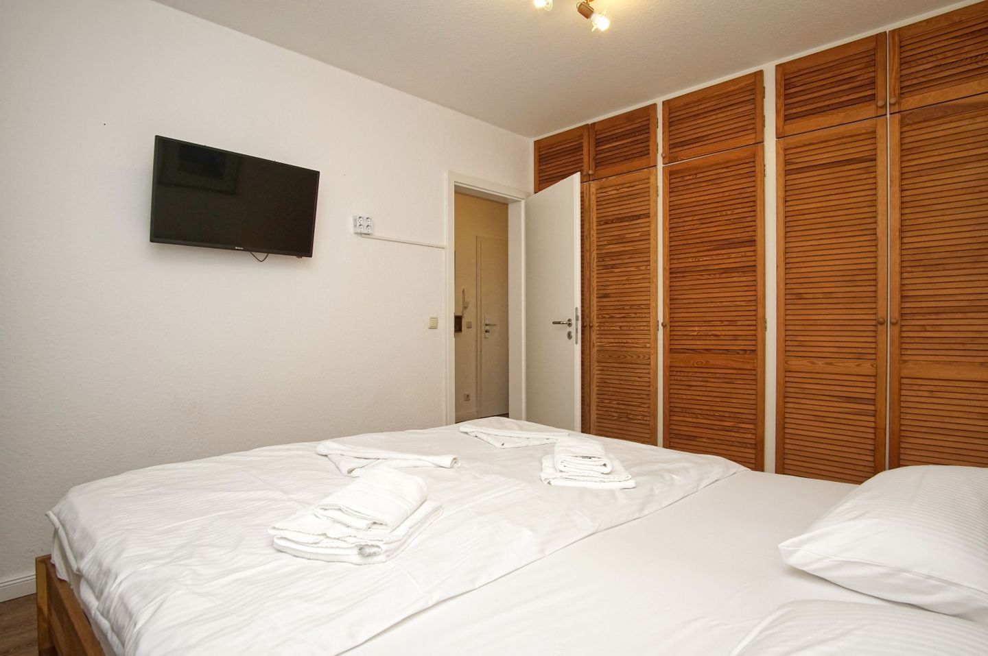 Une chambre à coucher avec un lit, un téléviseur fixé au mur et une armoire en bois.