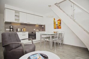 Une cuisine moderne avec des meubles blancs, un coin repas doté d’une table et de chaises en verre, et un escalier avec une rampe blanche.