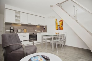 A modern kitchen with white cabinets, a dining area with a glass table and chairs, and a staircase with a white railing.