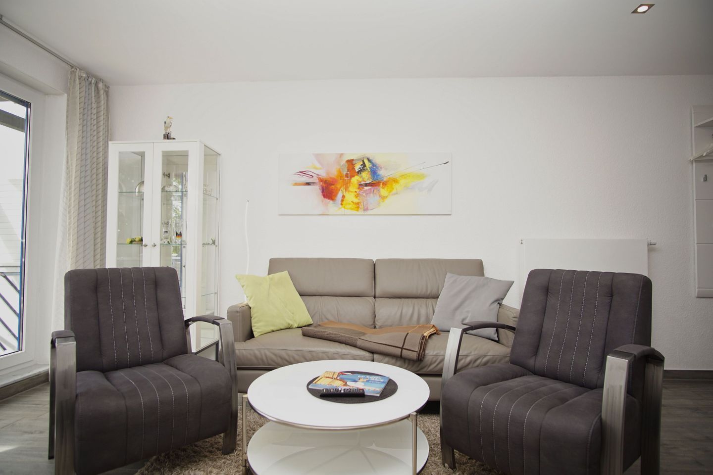 A modern living room with a grey sofa, two armchairs, a coffee table, and a glass cabinet.