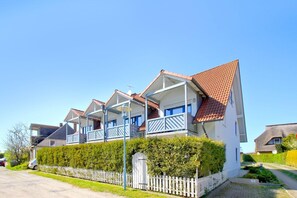 A row of white houses with red roofs and blue balconies, surrounded by a white picket fence and greenery. - Cozy vacation apartment near the harbor - FeWos am Hochzeitsberg FeWo 10 - FeWos (Breege)