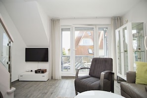 A modern living room with a flat-screen TV, a comfortable armchair, a sofa, and a glass cabinet.