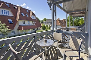 Ein Balkon mit Gartenmöbeln, Blick auf Nachbarhäuser und einem wolkenlosen Himmel.