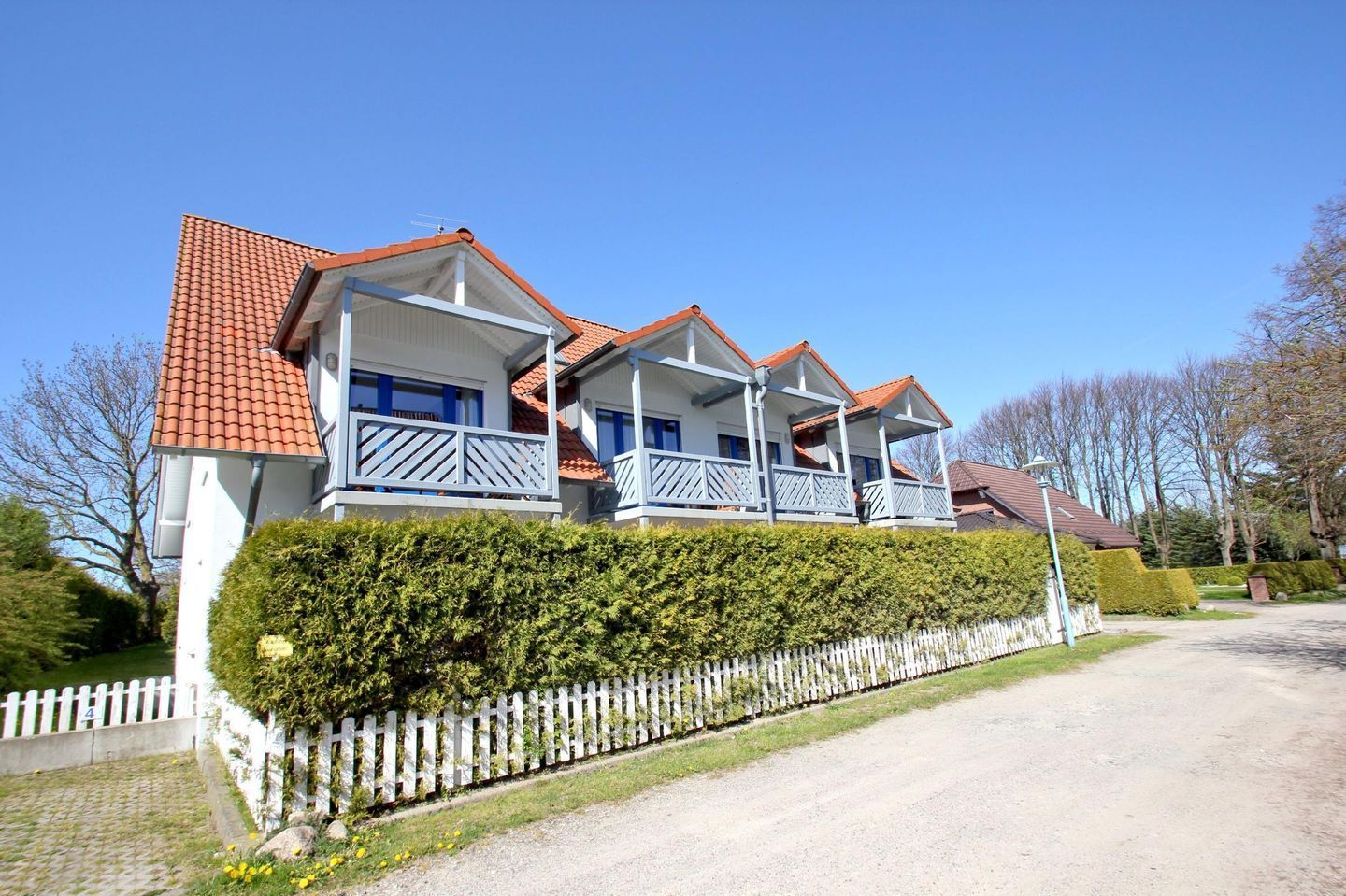 A two-story house with a red-tiled roof, white exterior walls, and a white picket fence.