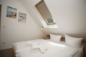 A bedroom with a skylight, a bed with white linens, and two wall-mounted pictures.