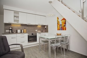 A modern kitchen with white cabinets, a built-in oven, and a dining area with a glass table and chairs.