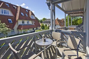 A balcony with outdoor furniture, a view of neighboring houses, and a clear sky.