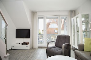 A modern living room with a flat-screen TV, a comfortable armchair, a sofa, and a glass cabinet.