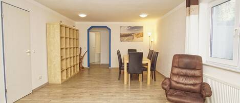 A modern living room with a brown leather chair, a dining area with a table and chairs, and a bookshelf.