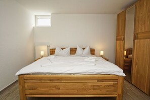 A bedroom with a wooden bed, white bedding, two bedside lamps, a small window, and a wooden wardrobe.