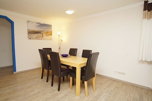 A dining area with a wooden table and black chairs, a blue bowl on the table, and a painting on the wall. - Cozy vacation apartment near the harbor - FeWos am Hochzeitsberg FeWo 17 - FeWos (Breege)