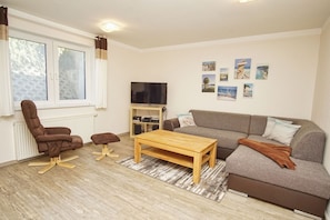 A living room with a brown leather chair, a grey sofa, a wooden coffee table, and a TV on a stand.