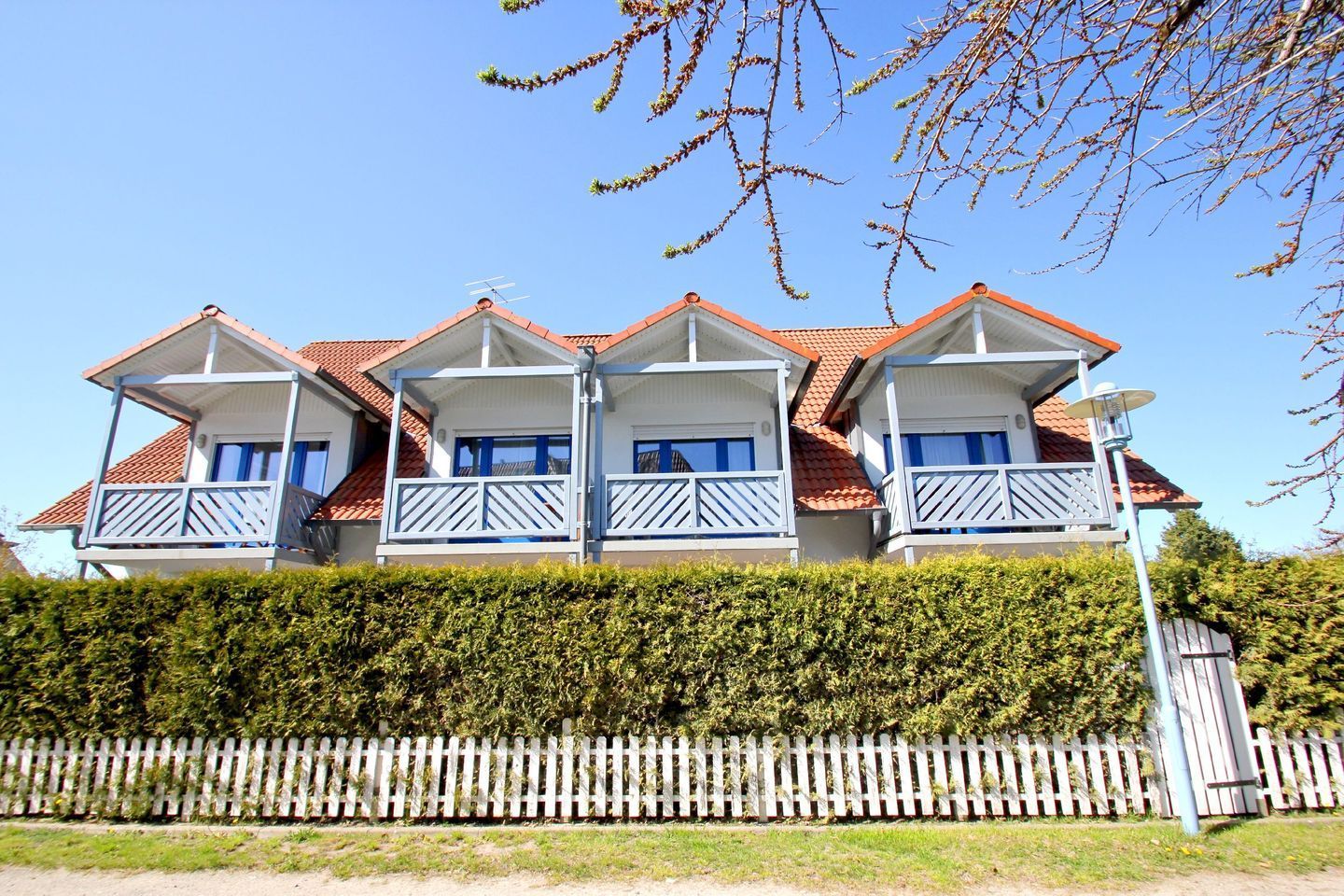 A three-story house with a red-tiled roof, multiple balconies, and a white picket fence.
