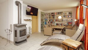 Een woonkamer met een open haard, bank, tafel en een boekenkast.