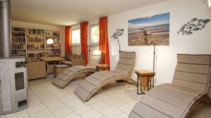 Een gezellige woonkamer met een open haard, comfortabele zitplaatsen, een boekenkast en een schilderij met een strandthema.