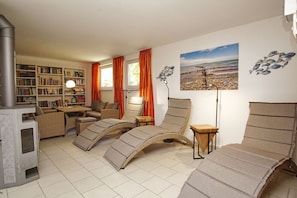 A cozy living room with a fireplace, comfortable seating, a bookshelf, and a beach-themed wall art.